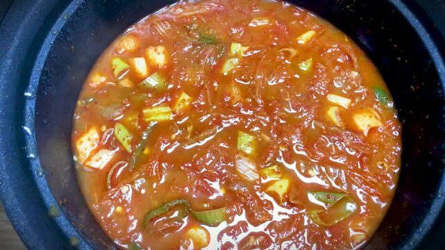 Hot kimchi jjigae Korean kimchi stew bubbles in a large metal bowl.