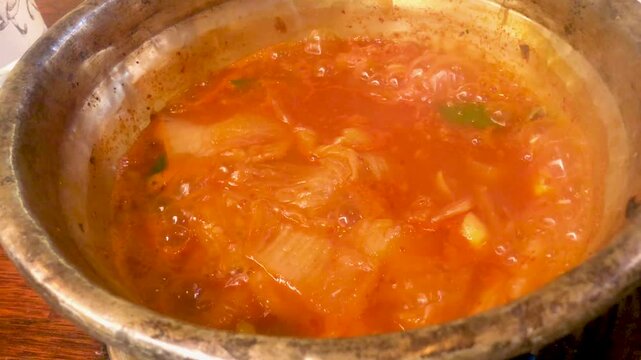 Hot kimchi jjigae Korean kimchi stew bubbles in a large metal bowl.