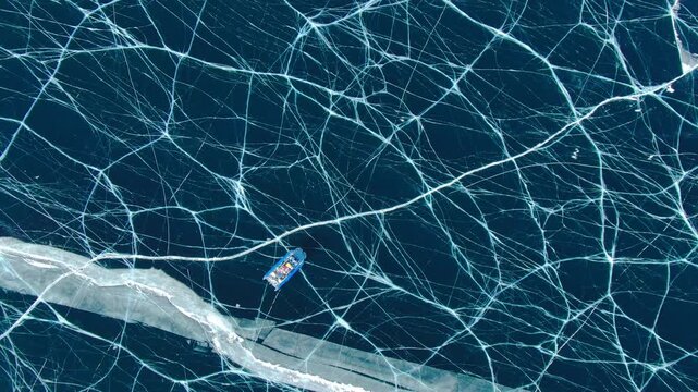 Hovercraft moving drifting sliding over cracked deep dark blue ice on frozen Baikal lake. Aerial drone top view of vehicle traveling. Winter expedition and extreme adventure in cold climate.