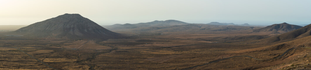 Fototapeta premium A panoramic view from Mirador de Vallebron shows arid plains and Montana Tindaya rising on the right, with distant mountains along the horizon, Fuerteventura, Canary Islands, Spain.
