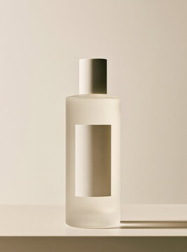 Frosted glass cosmetic bottle mockup with blank label on white shelf against beige background.