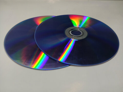 Two blank compact discs showing colorful rainbow light reflections on a white background