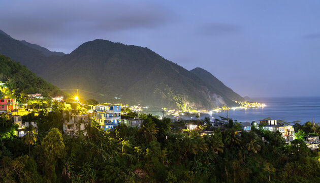 A beautiful night view of a coastal village nestled in the lush green hills of Dominica, Caribbean