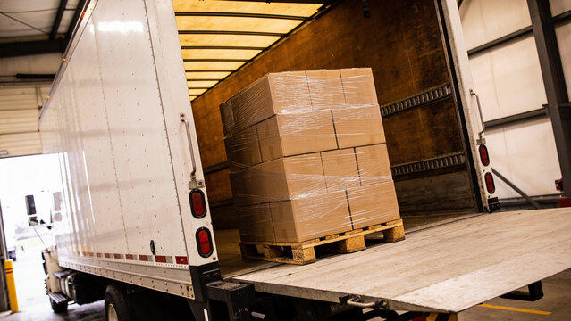 Pallet of stacked cardboard boxes wrapped in plastic on a truck lift gate inside a loading dock, logistics and freight shipping concept.