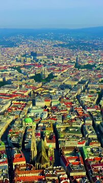Vertical video. Vienna, Austria. St. Stephen's Cathedral (Stephansdom), its soaring Gothic south tower and steep multicolored tile roof dominating the historic city center, aerial panoramic view, cle