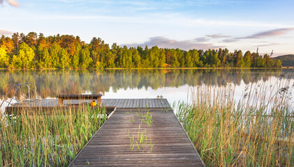 Obraz premium Calm lake with wooden pier, autumn foliage, and golden light