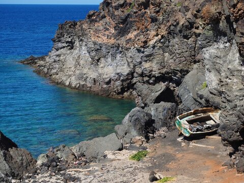 Small wooden fishing boat resting on volcanic rocky shore at Nika bay in Pantelleria