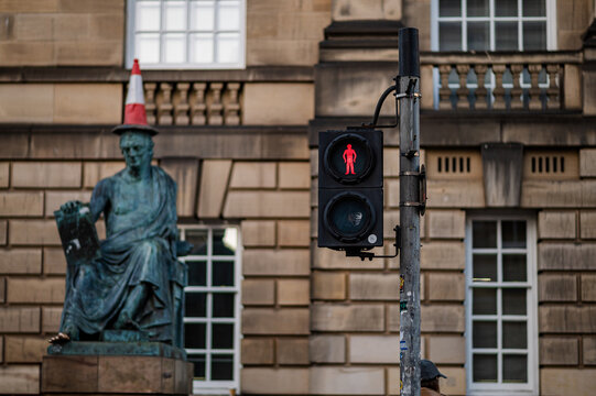 Red pedestrian signal beside statue wearing traffic cone