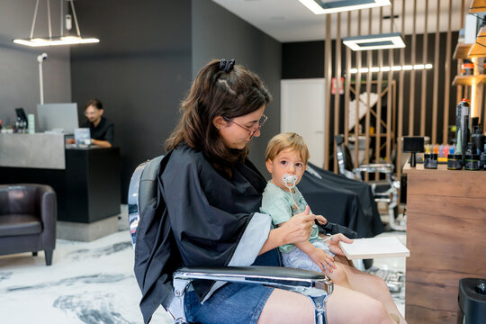 Mother holds toddler during haircut at modern barbershop
