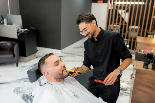 Barber trim beard of male client in modern barbershop