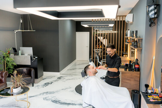 Barber grooming bearded client with comb in modern barbershop