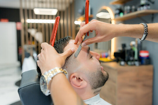 Barber shave client's temple with straight razor in barbershop
