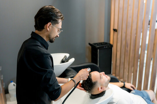 Barber wash client's hair in modern barbershop salon