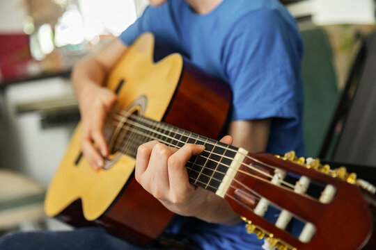 Teenager play acoustic guitar indoors in close-up