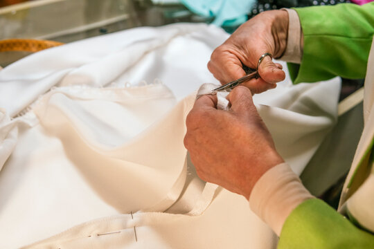 Dressmaker trims thread from handmade white garment