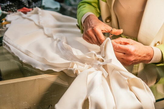 Dressmaker trim white fabric with scissors in workshop