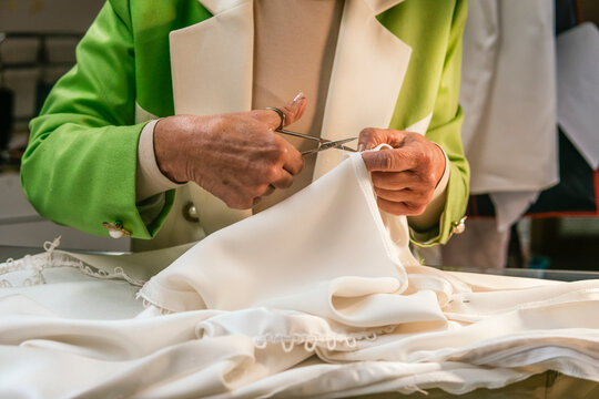 Dressmaker trim white fabric with scissors in workshop