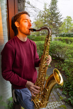 Man play saxophone outdoors beside garden window
