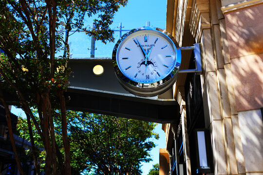 A close-up low-angle shot of a wall-mounted luxury Patek Philippe double-sided outdoor clock mounted on an elegant stone storefront building in Buckhead, Atlanta.