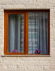 Obraz premium Wooden window frame with sheer curtains and purple flowers on windowsill