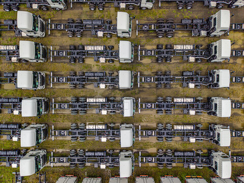 Aerial view of a new truck storage park with rows of white truck chassis parked on a grassy lot in Atsugi, Kanagawa, Japan.