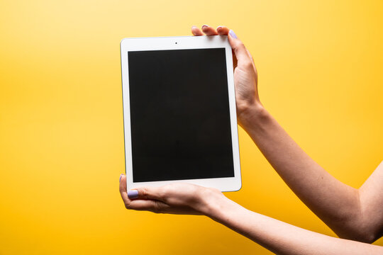 Woman hands hold tablet with blank screen on yellow background
