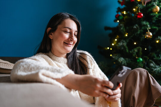 Woman use smartphone beside Christmas tree at home