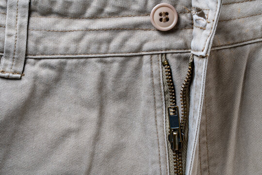 Khaki pants with open zipper. Closeup of beige cotton trousers featuring brown button and partially open metal zipper fly