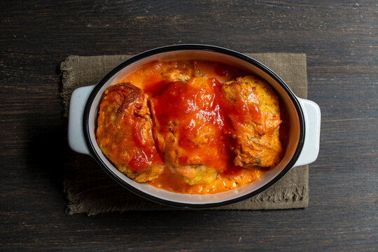 Baked cabbage rolls with tomato sauce, top view, closeup. Traditional stuffed cabbage rolls or cutlets baked in savory red tomato and sour cream sauce inside white ceramic dish on dark background