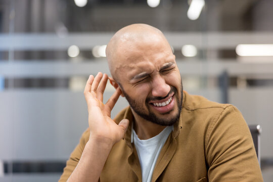 Ear pain and hearing loss, man suffering from tinnitus or earache in office environment, Professional male experiencing physical discomfort and sensitivity, health and wellness