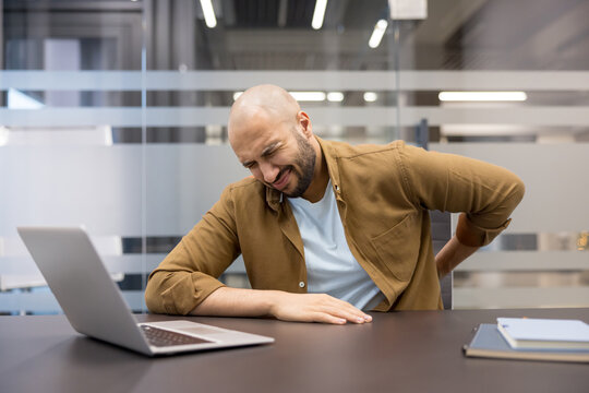 Back pain and office burnout, man suffering from physical discomfort while working on a laptop at his desk, Chronic strain and poor ergonomics in the workplace