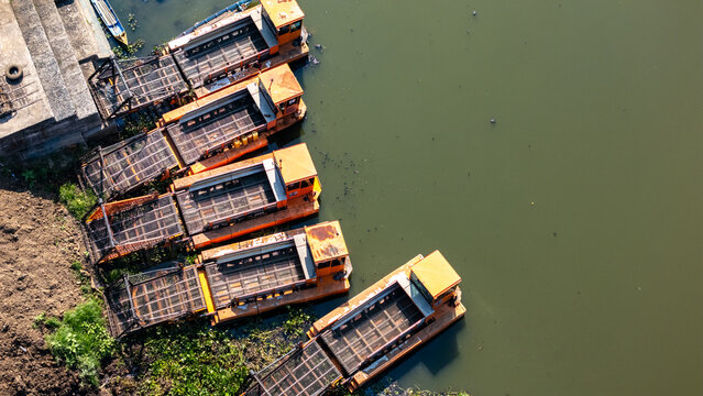 Aerial view of several orange industrial barges moored along a riverbank with calm water and muddy shore in Salatiga, Central Java, Indonesia.
