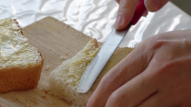 Close-up of a person spreading butter on a slice of bread with a knife. Simple food preparation at home, suitable for breakfast, cooking, bakery, sandwich and everyday lifestyle content.