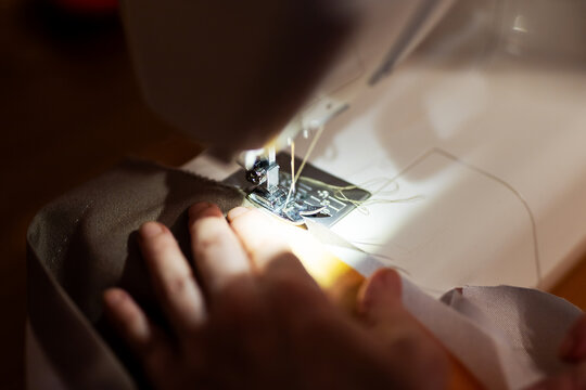 Close-up of hands guiding fabric through sewing machine needle during stitching