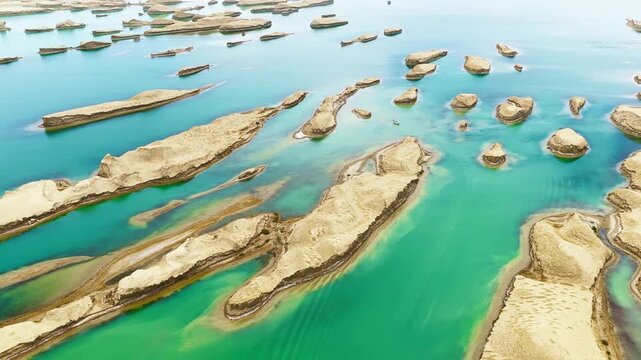 High angle shot of water yardang landforms surrounded by clear turquoise lake water under bright diffuse daylight in Qinghai, China.