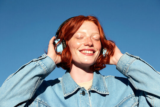 Cheerful Gen Z woman enjoy music with headphones outdoors