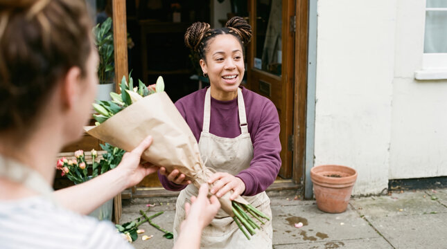 Florist handing flower bouquet to customer outside shop