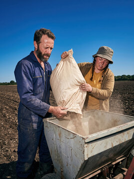 Farmers tipping a seed sack into a drill hopper