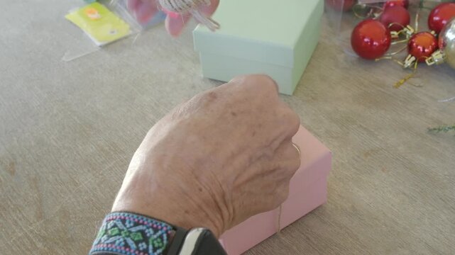 Elderly woman hands wrapping small pink gift box