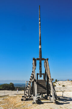 Front view, far distance of, a medieval rock throwing weapon, catapult with a blue sky and under mid-morning sunlight