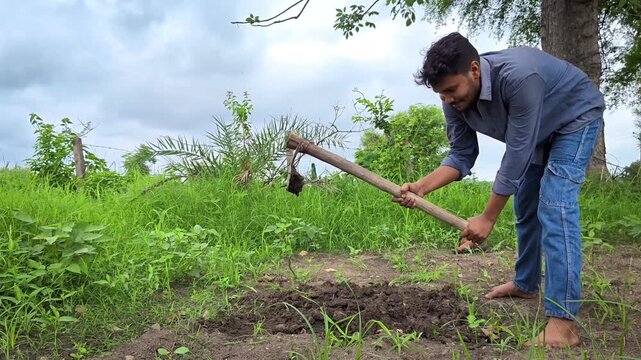 Young indian farmer digging soil with hoe tool for gardening pot