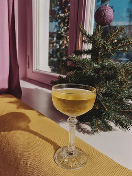 Golden cocktail sits beside a decorated Christmas tree near a sunlit window. Ideal for festive beverage, hospitality, and Christmas advertising.