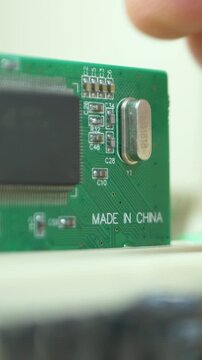 Tech specialist pushes PCI board into motherboard slot. Green surface with Made in China note. Electronic circuit card background. Computer repair and maintenance workshop