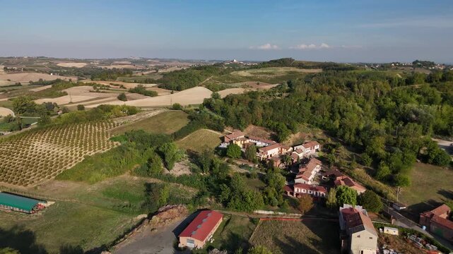 Aerial view of Italian hamlet with farmhouses, vineyard rows and rolling hills in Piedmont countryside at golden hour