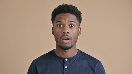 Fototapeta premium Surprised African American Man Expressing Shock and Astonishment with Wide Eyes and Open Mouth, Studio Portrait.