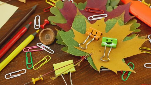Colorful binder clips with smiley faces on yellow green autumn leaves. Office essentials. Cozy creative workspace featuring colorful stationery. Pencils and paper clips, Back to school concept
