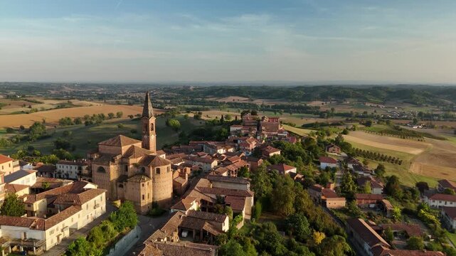 Aerial drone view of Tonco village rooftops and bell tower above rolling farmland at sunrise, Asti, Piedmont, Italy