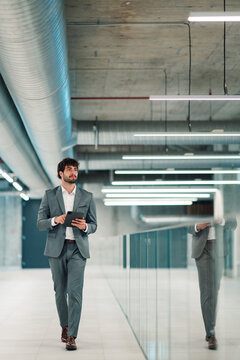 Businessman walking with a tablet in a modern office building, reflecting professional success and technology integration