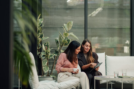 Businesswomen collaborating on a digital tablet during a casual meeting in a modern office lounge area