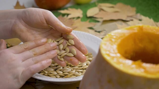 Pumpkin seeds glisten in bowl. Hand touches harvest symbol. Halloween crafted with care. Lantern carved from same fruit. Seeds offer reminder of seasons richness and family warmth
